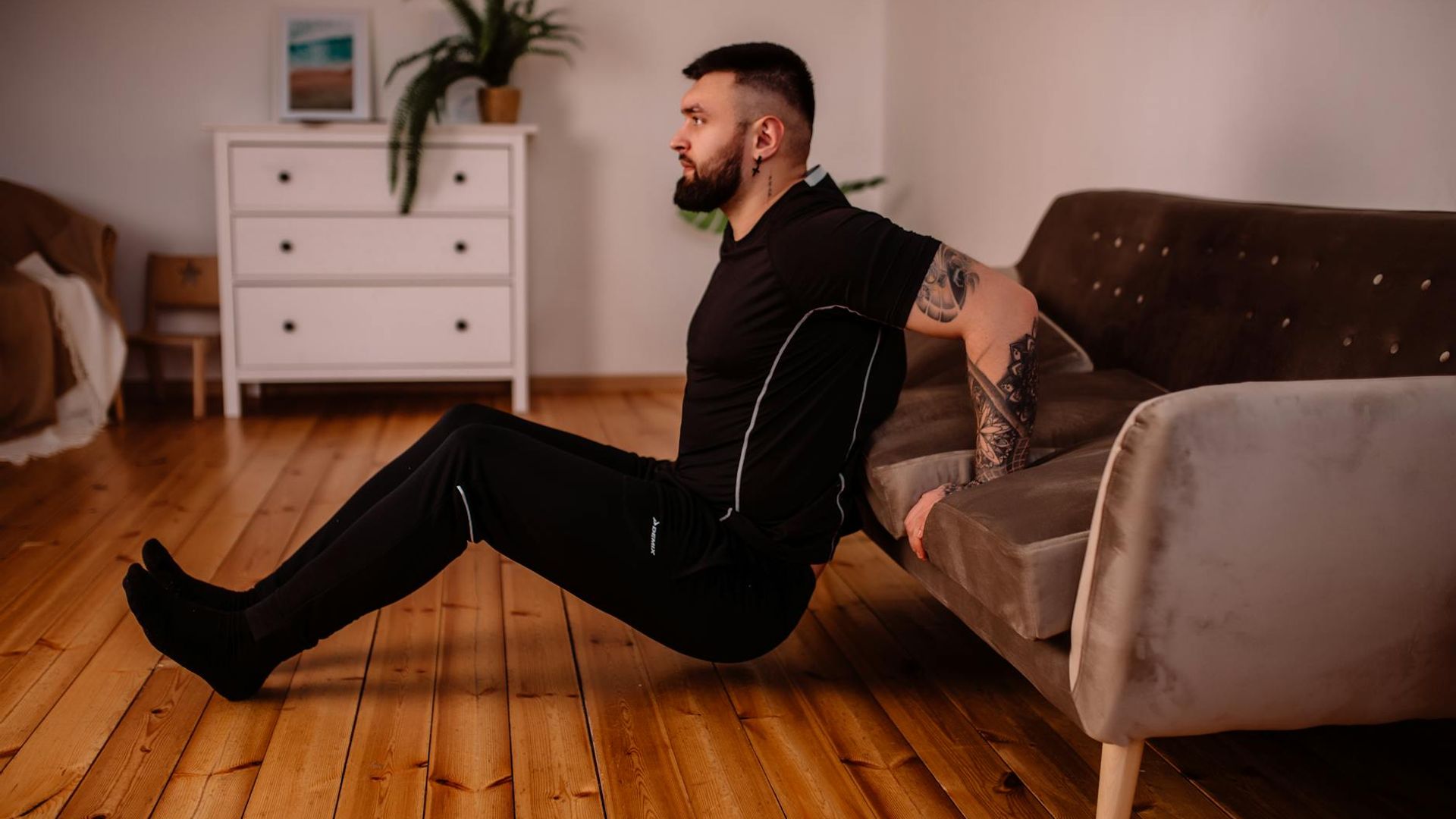 Man in a focused stance performing a bodyweight exercise in a minimalist dark room.